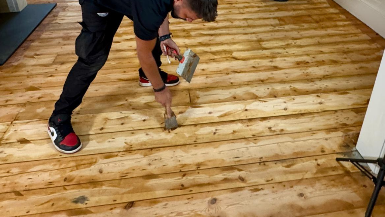 A professional in West Kensington securing loose boards on a solid pine wooden floor with a hammer, preparing for wood floor sanding.