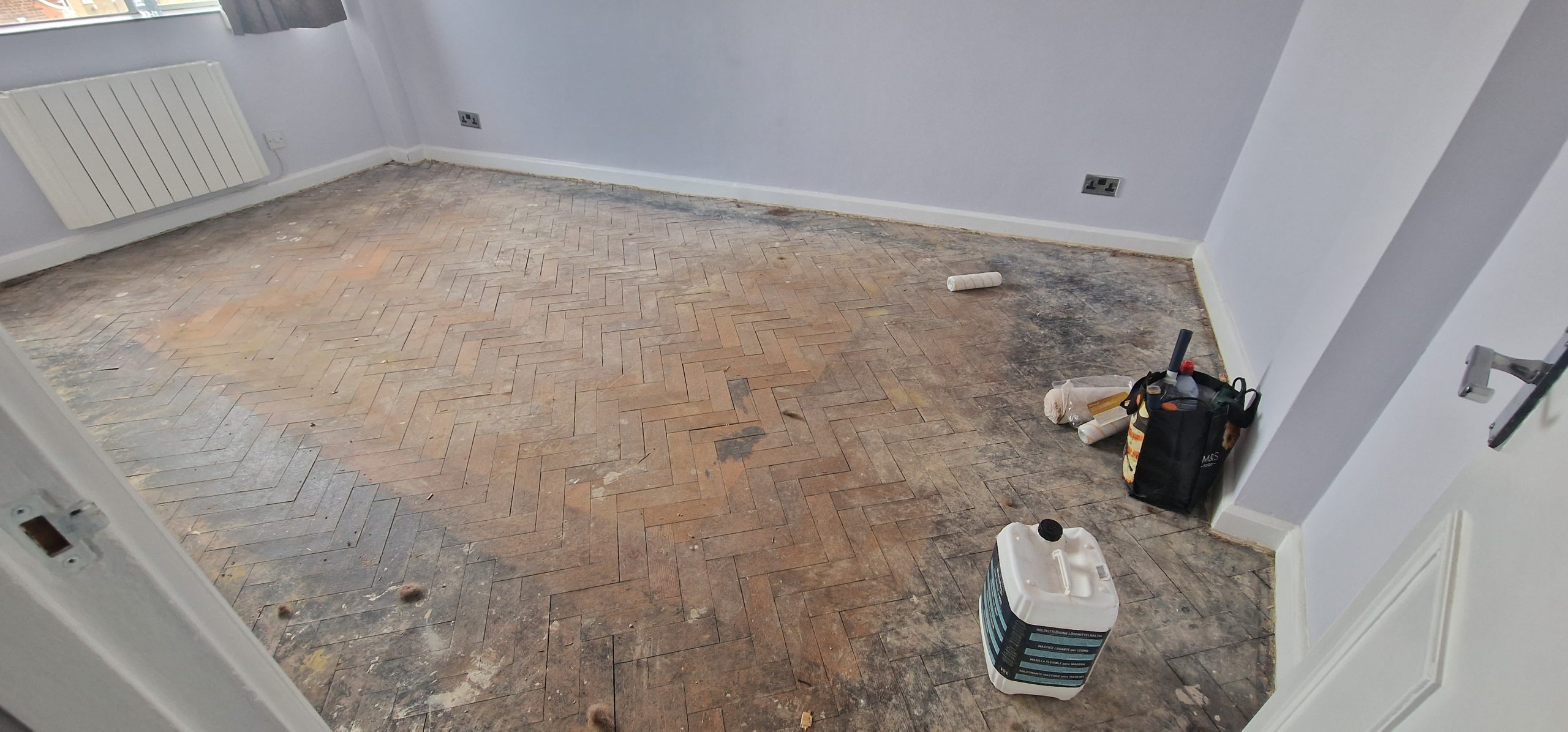 Room in West Kensington awaiting Parquet Floor Repairs, showing a worn oak herringbone parquet floor before sanding and restoration.
