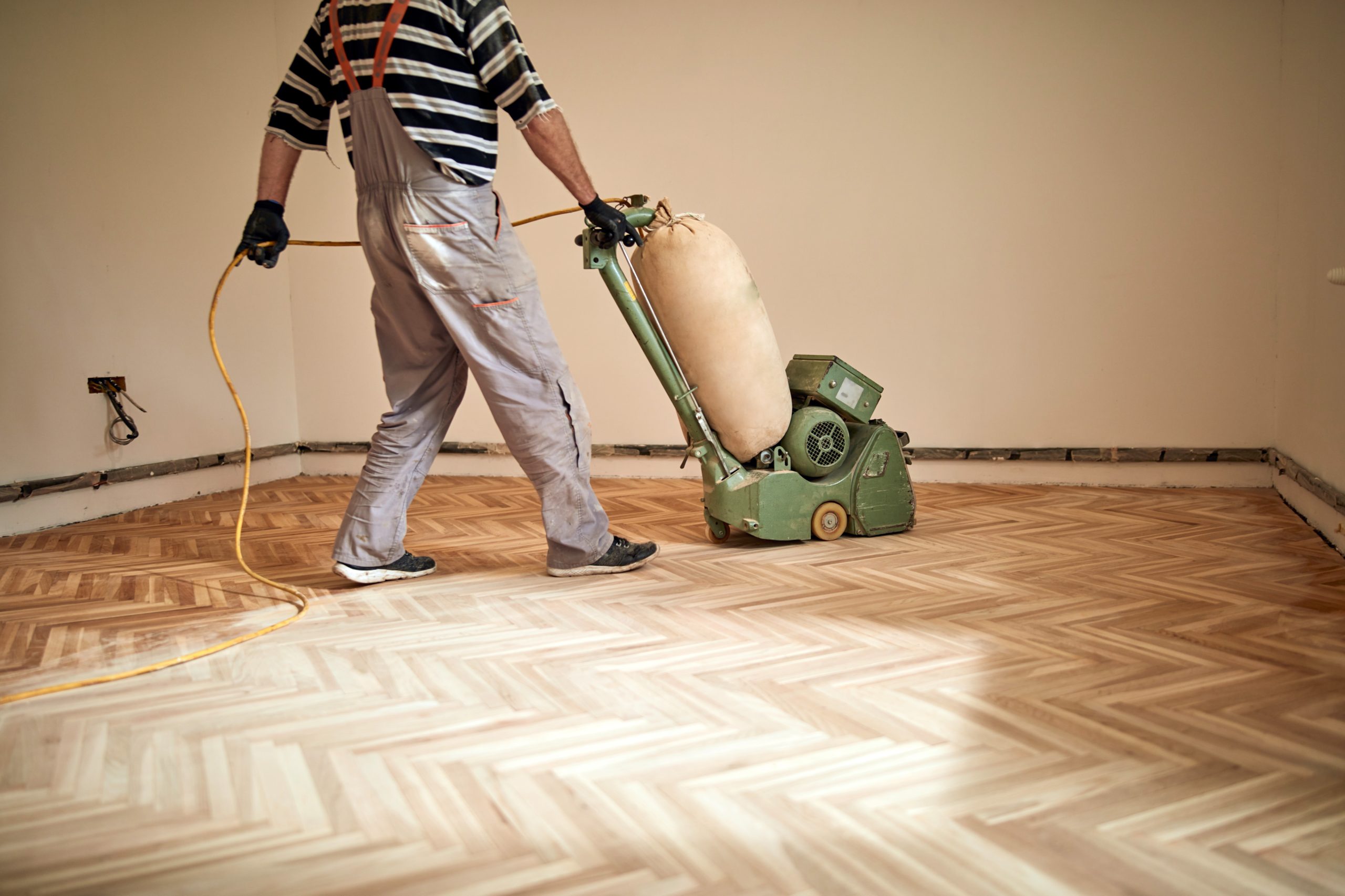 Professional carrying out Parquet Floor Repairs in West Kensington using a sanding machine on an oak herringbone parquet floor.