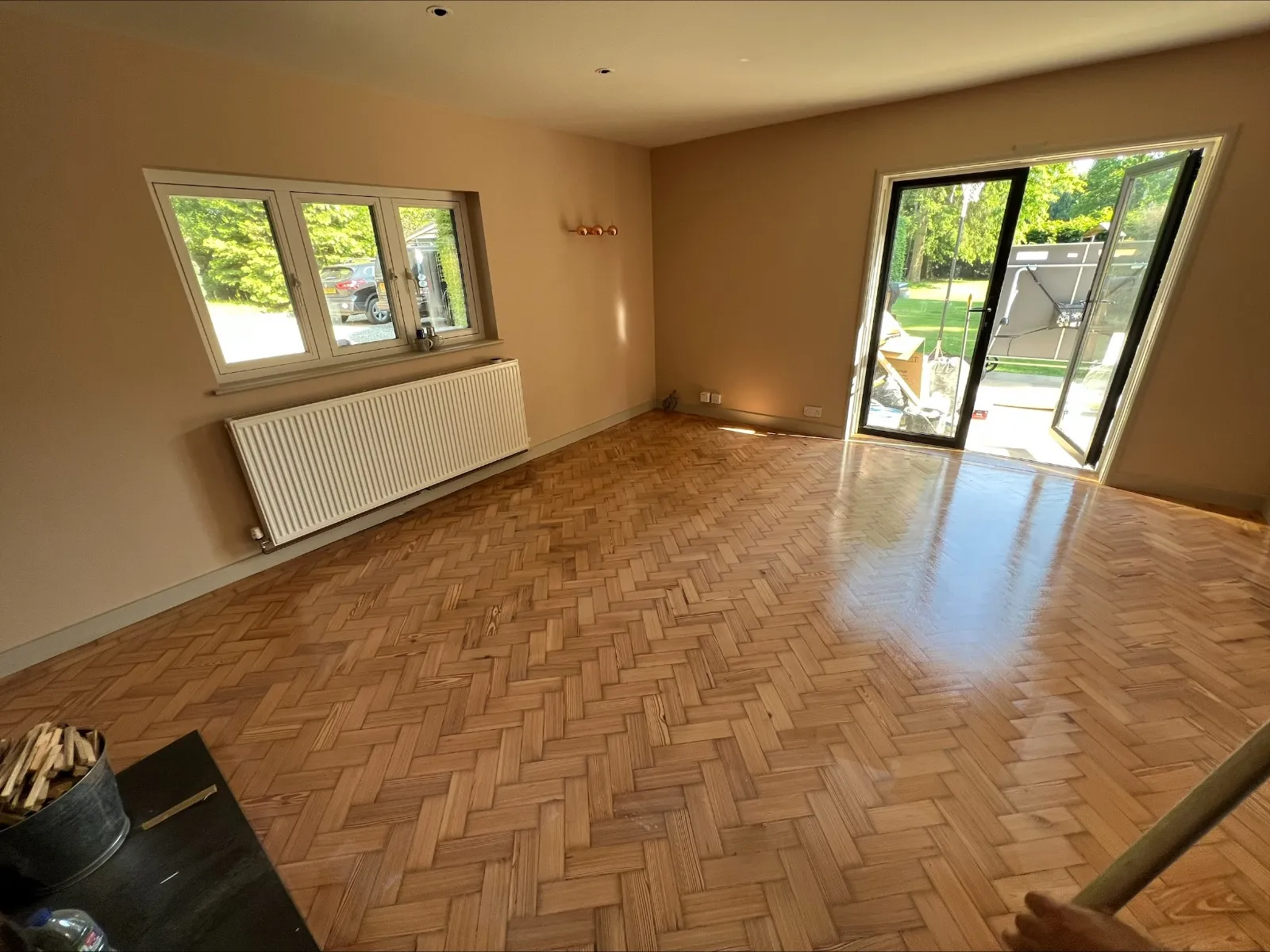 Parquet Floor Sanding in West Kensington – restored light oak herringbone parquet living room floor with a smooth, glossy finish and sunlight from garden doors.