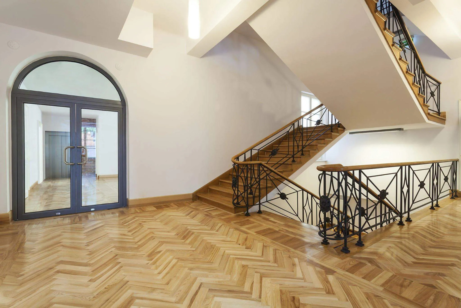 Parquet Floor Sanding in westkensington – beautifully restored oak herringbone parquet floor in a bright hallway with matching wooden stairs and iron balustrade.