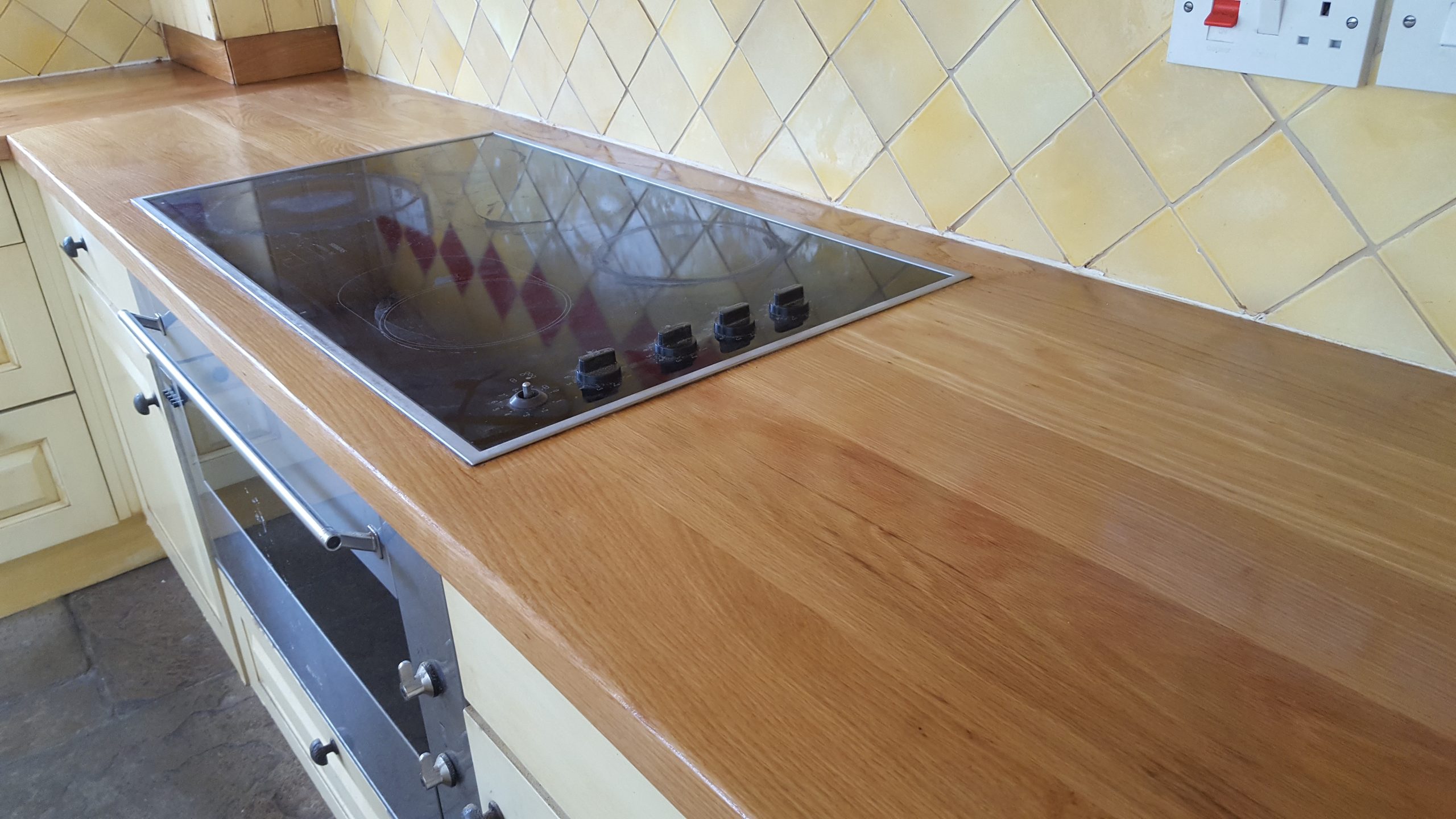 Worktop Refinishing in West Kensington – restored solid oak wooden kitchen worktop around electric hob with natural stone tile floor