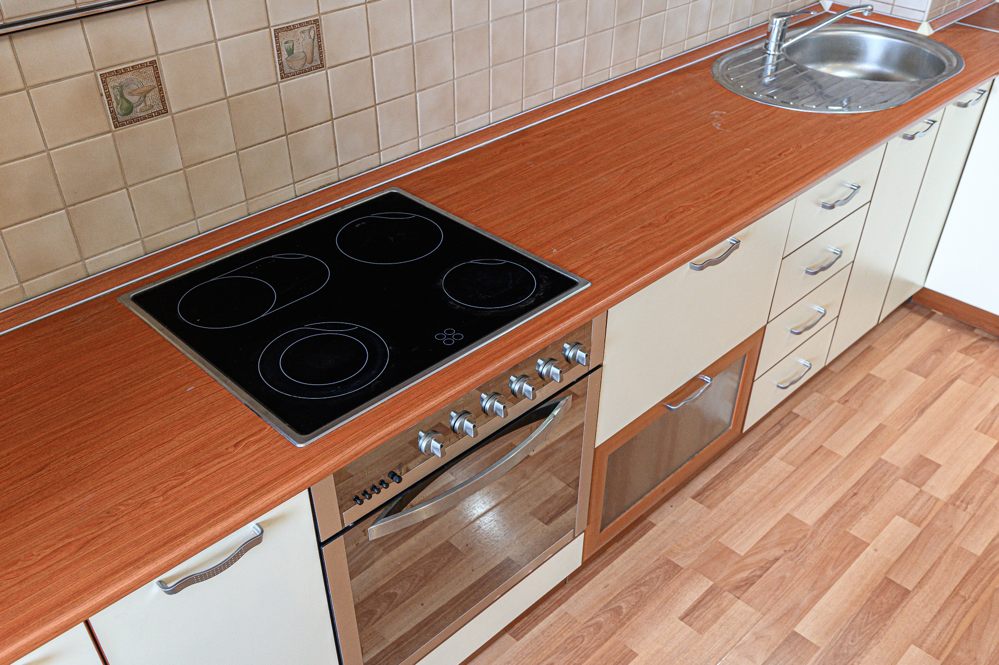 Worktop Refinishing in West Kensington – modern kitchen with restored wood-effect laminate worktop and matching oak-effect laminate wood floor around hob and sink