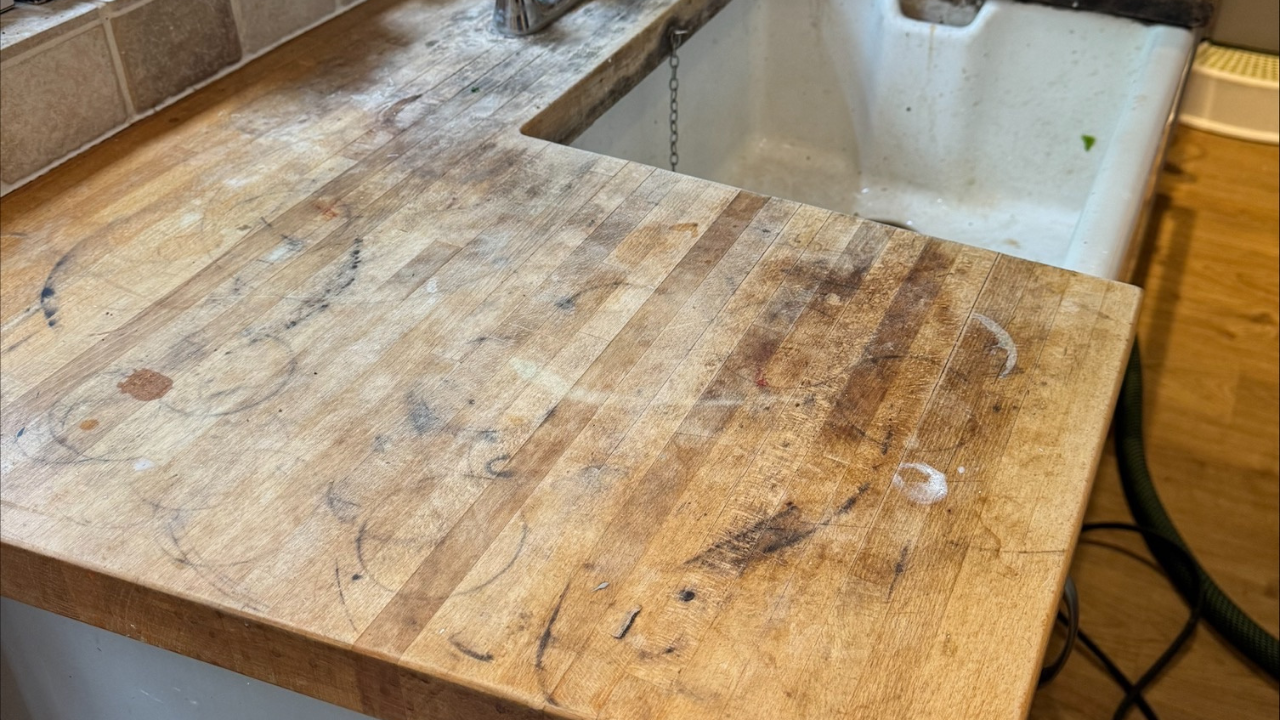 Worktop Refinishing in West Kensington – worn oak butcher block wooden kitchen worktop beside Belfast sink above an oak plank wood floor